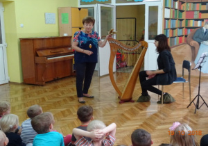 Dwie kobiety prezentują dzieciom instrument - harfę.